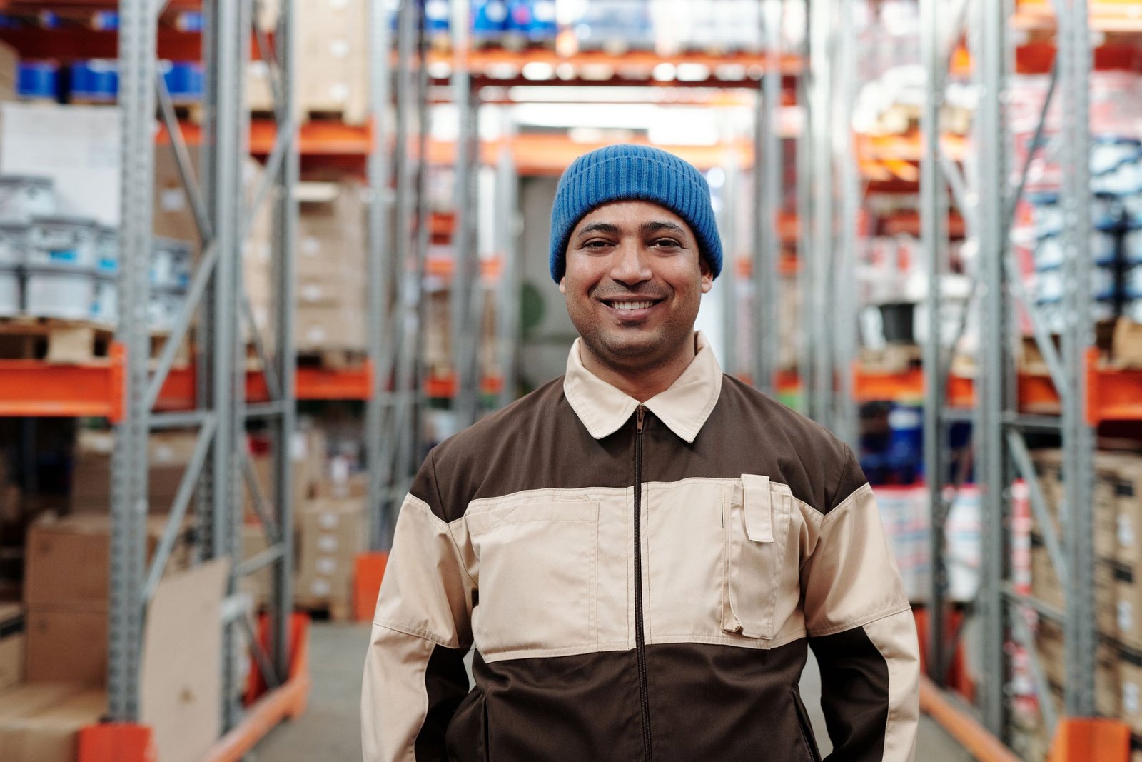 Smiling warehouse worker in a work jacket between high racks