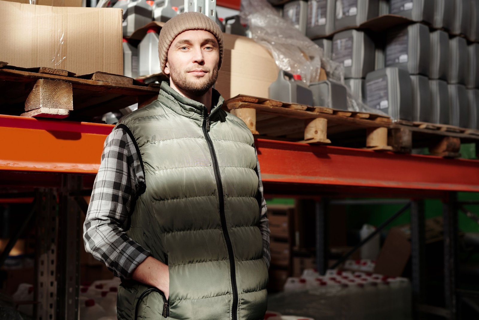 Worker in a gilet and beanie in front of warehouse racks