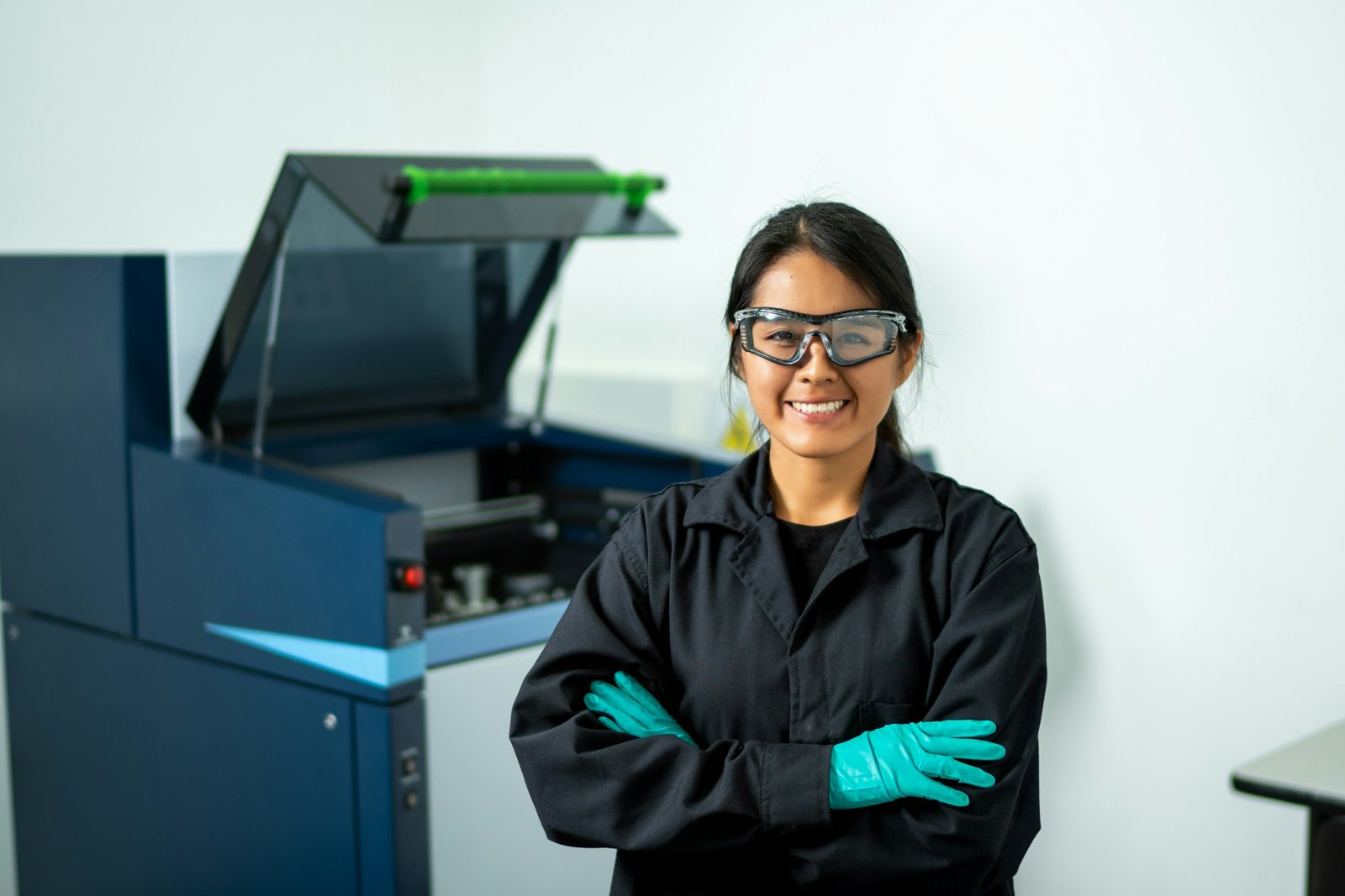 Smiling worker in safety goggles and gloves in front of a machine